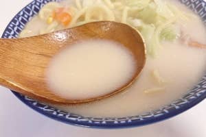 和風のどんぶりに入ったラーメン。木のスプーンがスープをすくう。野菜がトッピングされています。