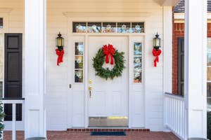 Front door decorated with a green wreath and red bow, flanked by red-bowed lanterns, conveying a festive, holiday ambiance